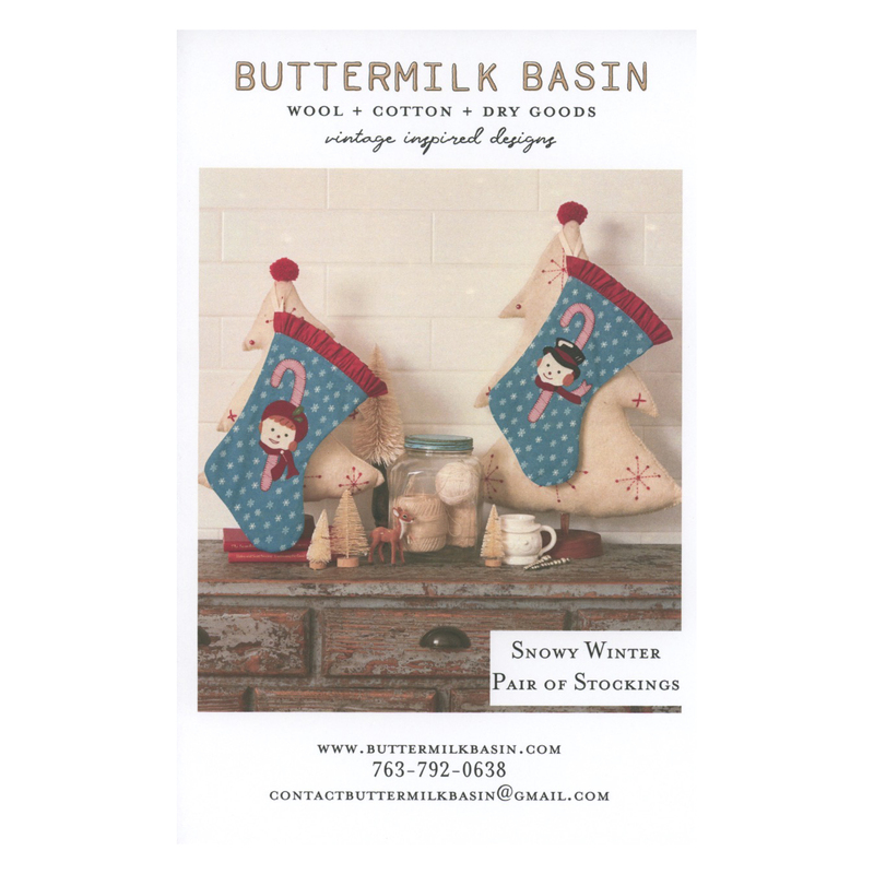 Front cover of the pattern showing the two completed stockings staged above a rustic wood desk, surrounded by winter themed trinkets.