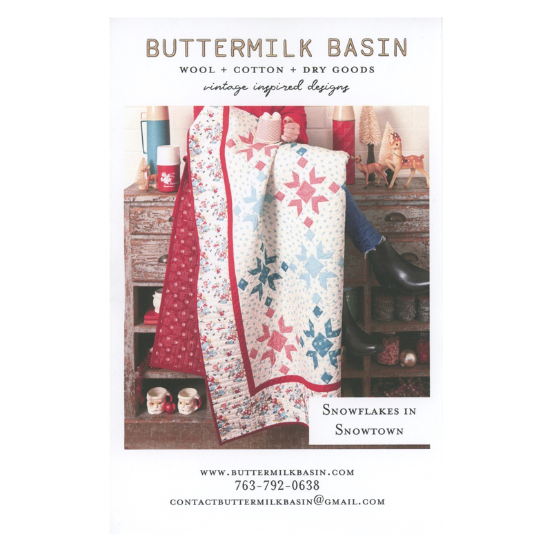 Front cover of the pattern, showing someone sitting on a rustic wooden desk and holding the finished quilt, draped to show about half of the quilt.