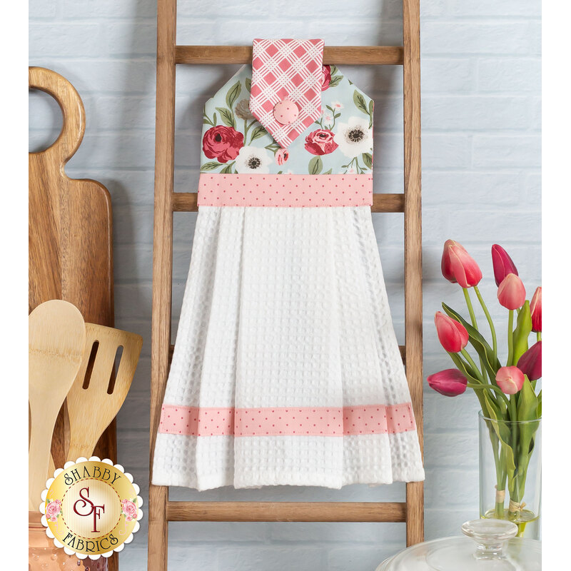 Photo of a hanging towel on a small ladder leaning against a wall with kitchen utensils, a cutting board, and tulips in the background