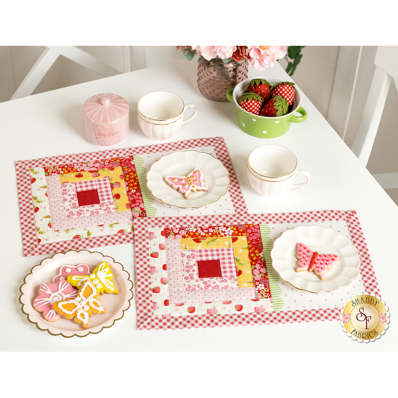 The two completed June placemats, colored in bright pink, red, white, and yellow, staged on a white table with coordinating decor. On white scalloped plates sit beautifully frosted flower and butterfly cookies.