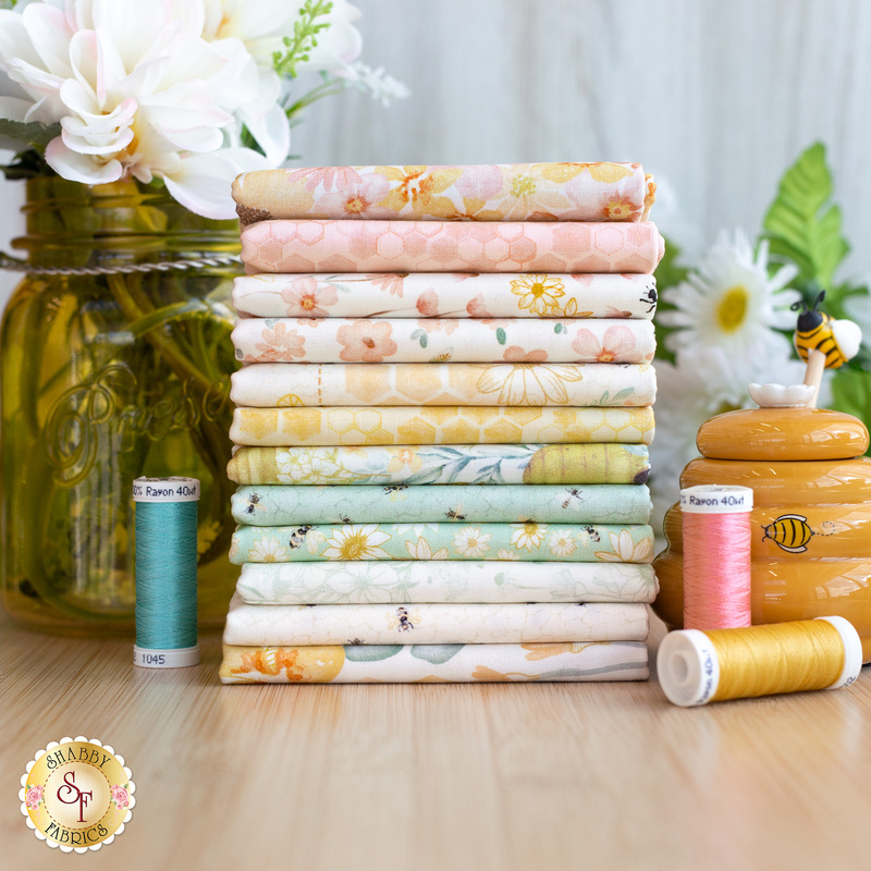 A stack of Home Sweet Home fabric surrounded by flowers and a beehive.