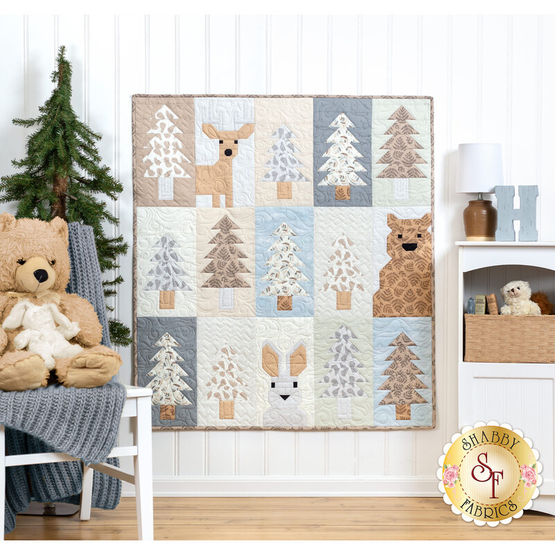 The completed Lookout quilt in soothing neutrals, staged on a white paneled wall beside coordinating furniture and stuffed animals.
