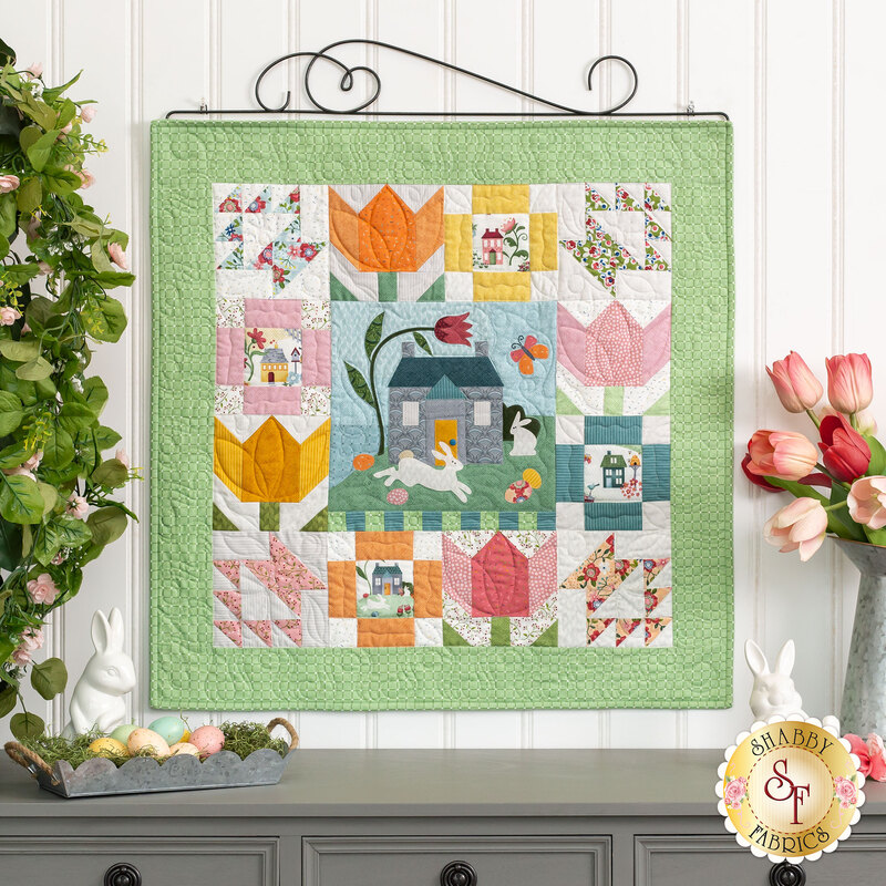 A small easter themed fabric wall hanging displayed on a scrolled craft holder against a white shiplap wall