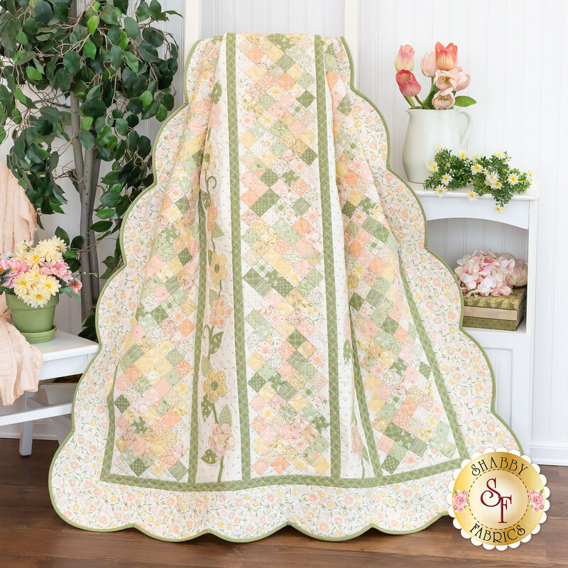 The completed Flower Girl quilt colored in cream, light pink, grass green, and sunshine yellow, artfully draped and staged with coordinating furniture.
