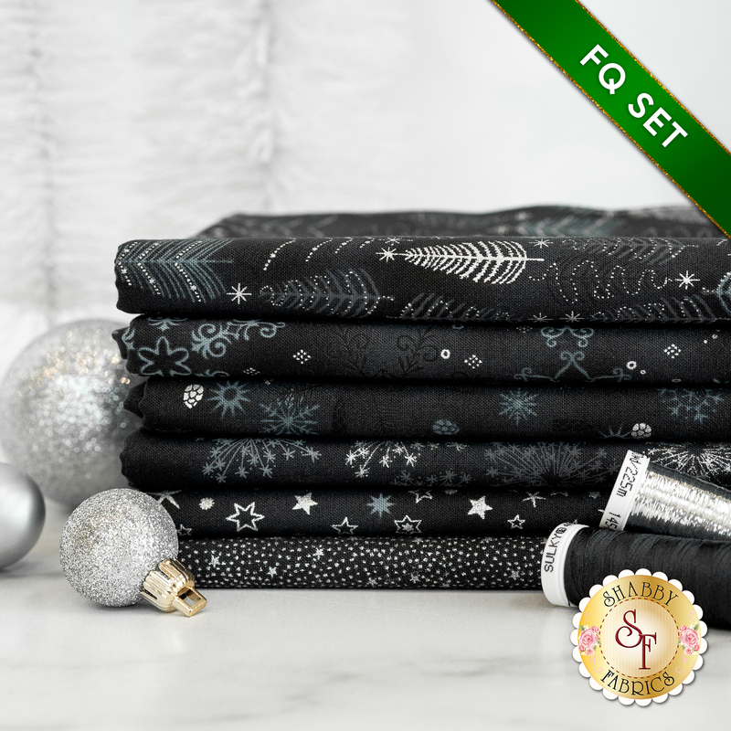 A photograph of the stacked fat quarters included in the Black/Silver set, staged with black thread and sparkling silver ornaments.