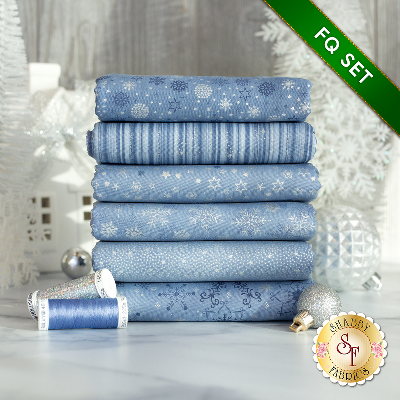 A photograph of the stacked fat quarters included in the Light Blue/Silver set, staged with cornflower blue and silver holoshimmer thread as well as sparkling white decor and ornaments.
