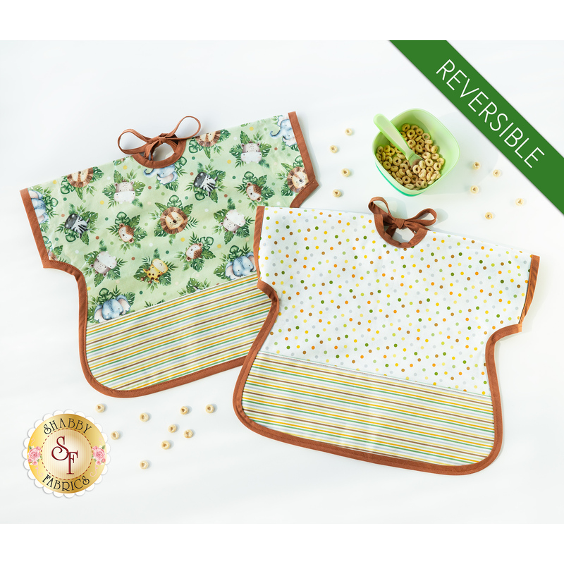 Two of the Toddler Bibs demonstrating the reversible feature, colored in green, cream, and brown fabrics, staged with a green bowl with cereal on a white background.
