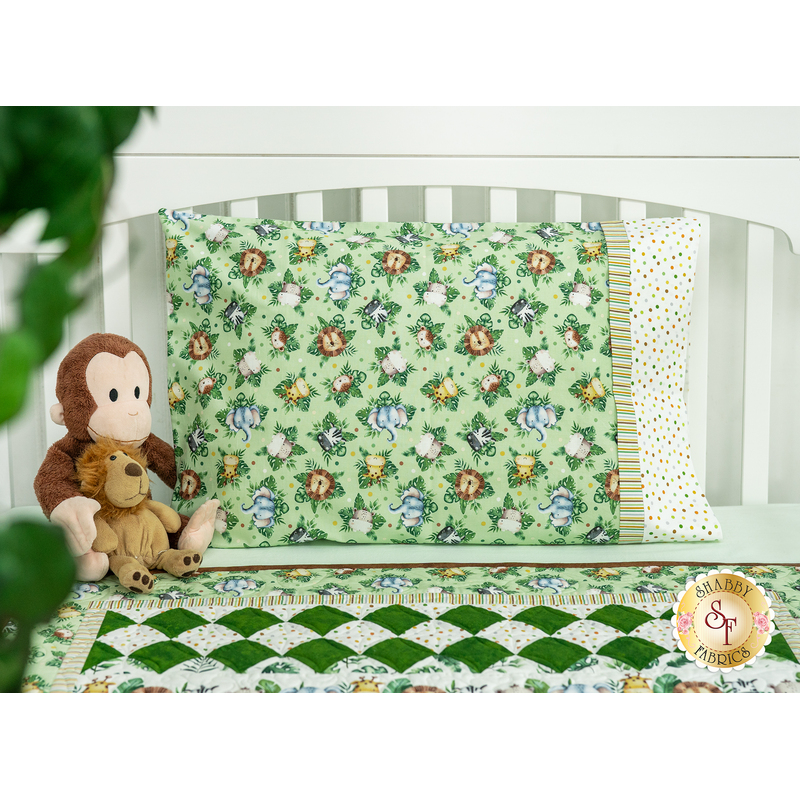 The completed magic pillowcase in Wee Safari fabrics, on display on a bed with the Little Pathways Quilt as well as a stuffed monkey and stuffed lion toy.