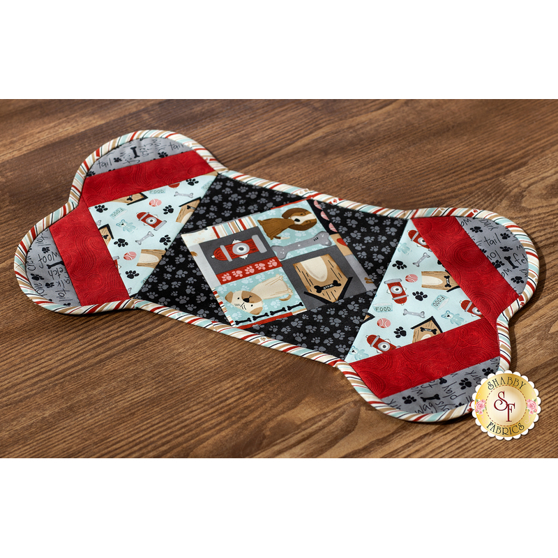 Photograph of the completed pet placemat in red, blue, black and gray fabrics from the Paw-sitively Awesome collection, staged on a hard wood floor.