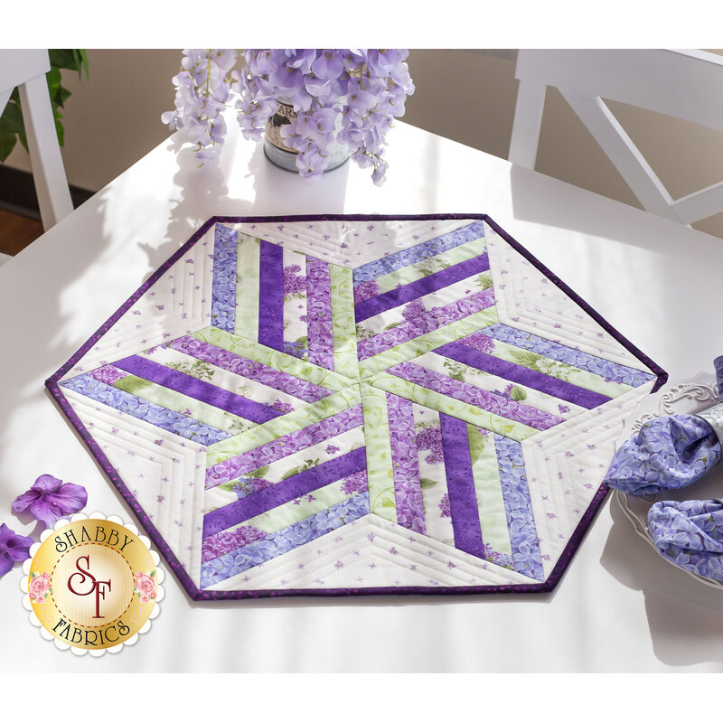 A shot of the completed Bloomerang Table Topper, staged on a white table with coordinating cloth napkins and purple flowers. Sunlight from the window illuminates the vibrant colors of the topper.