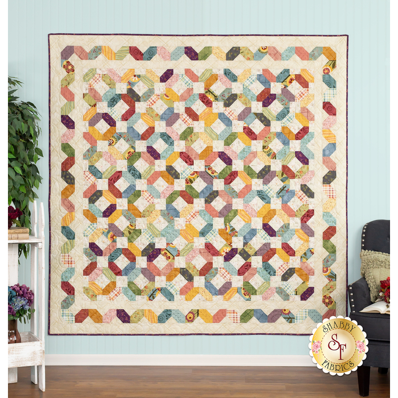 The completed Garden Path quilt colored in Gift of Grateful Praise, a rainbow of vibrant earth tones. Hung on a blue paneled wall, the quilt is staged with coordinating furniture and matching decor.