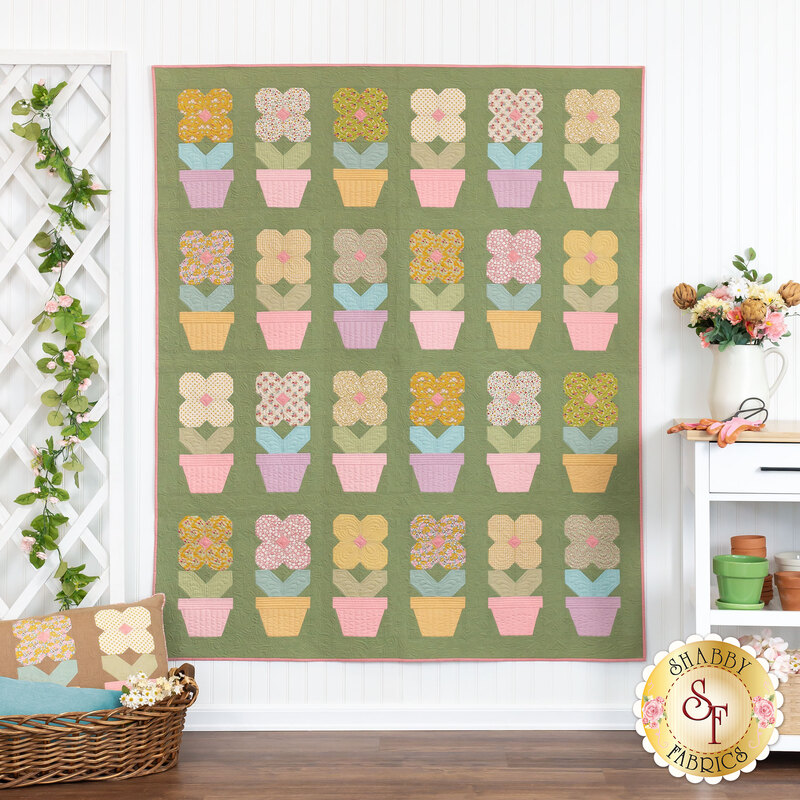 The completed Potted Flowers in Creating Memories, a palette of grass green, pink, yellow, and blue. The quilt is hung on a white paneled wall and staged with coordinating furniture and decor.