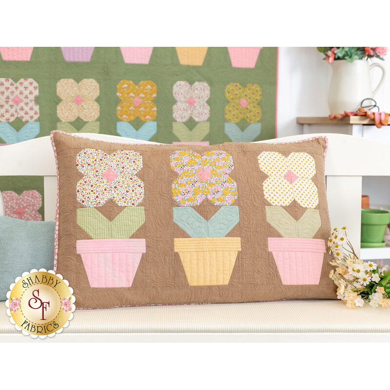 The completed Potted Flowers Pillow, staged on a white loveseat with coordinating flowers and decor. In the background, the Potted Flowers Quilt hangs on the wall.