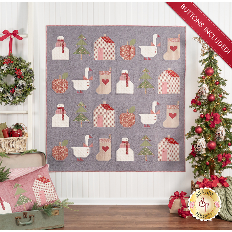 The completed Christmas Calendar quilt in gray, green, red, white, and cream. The quilt is hung on a white paneled wall and staged with Christmas decor. The red Winter Pillow makes an appearance in the lower left hand corner.