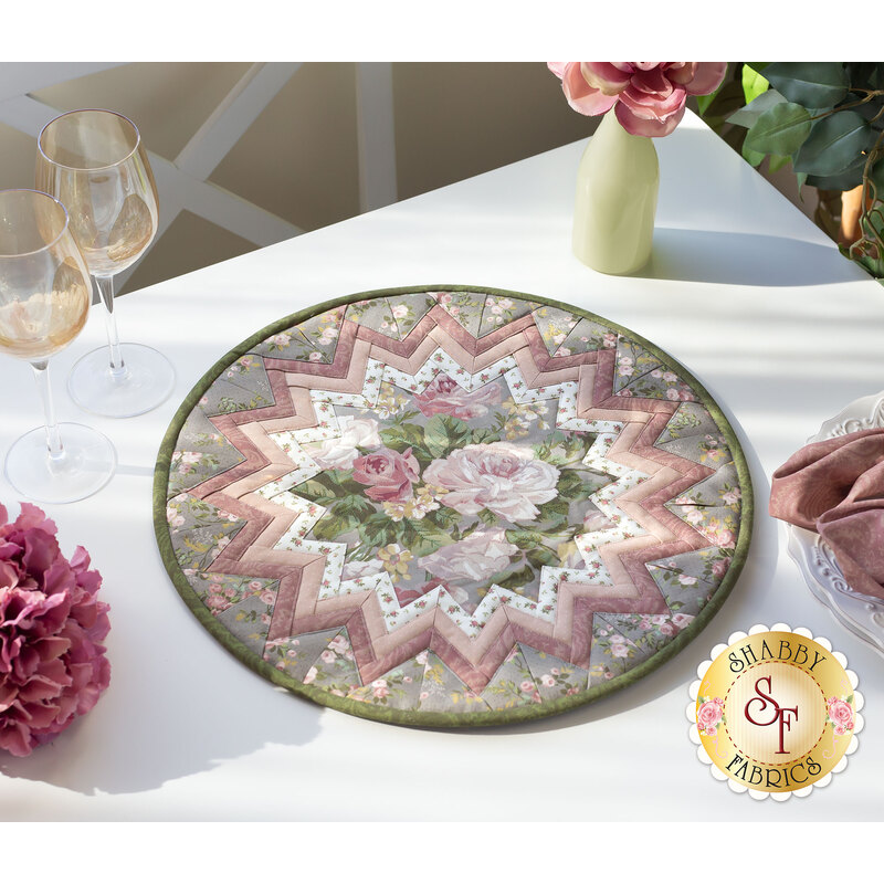 The completed Point of View Folded Star Table Topper, colored in the First Blush collection. The topper is staged on a white table with coordinating flowers and wine glasses.