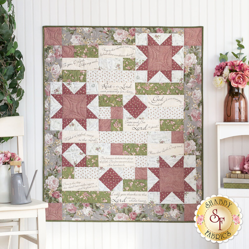 The completed Comfort of Psalms Quilt, colored in soothing cream, gray, green, and burgundy. The quilt is hung on a white paneled wall and staged with coordinating furniture and decor.