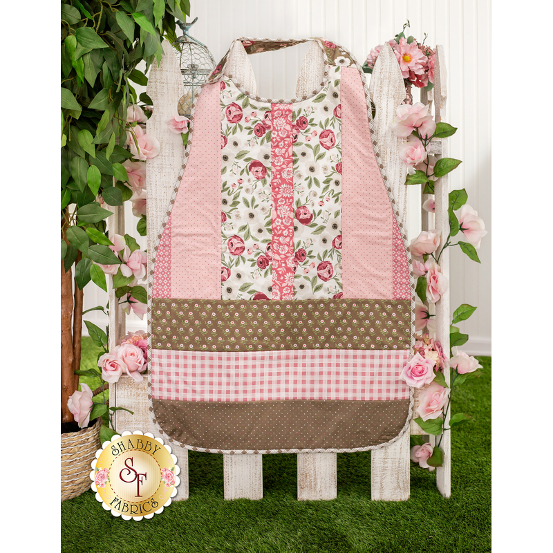 The completed pink Clothing Coverall, colored in baby pink, chocolate brown, and floral white. The coverall is staged on a white picket fence with matching pink roses and a leafy houseplant.
