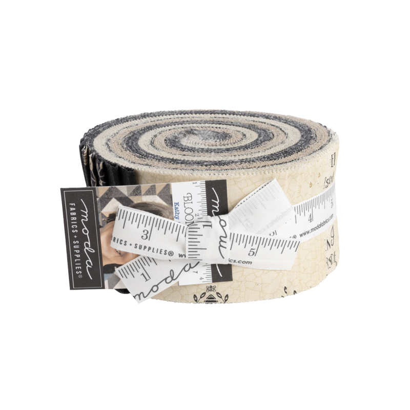 A spiraled roll of tan, cream, and black floral fabrics wrapped in a white ruler ribbon by Moda Fabrics