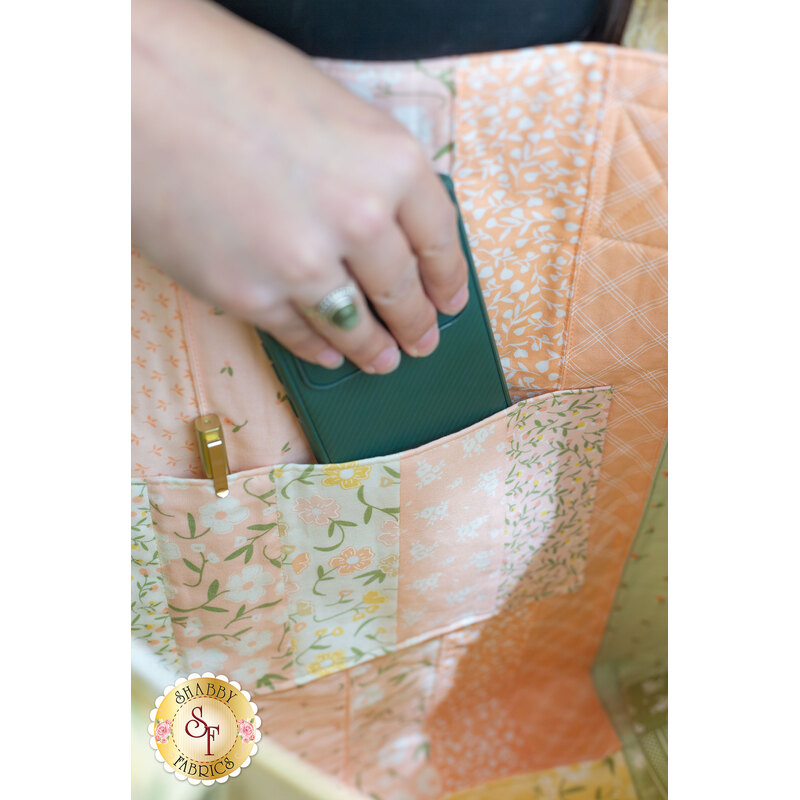 A model puts away a phone into the completed Flower Girl Jelly Roll Tote, demonstrating the patchwork of the project as well as the roominess of the project.