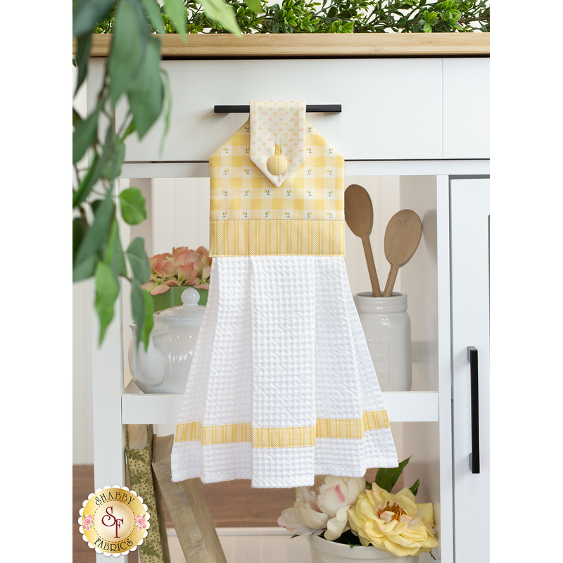 The completed hanging towel in yellow, hung from a kitchen drawer and staged with coordinating decor and greenery.