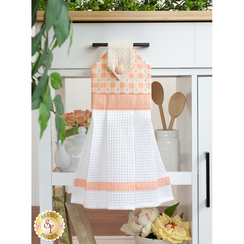 The completed hanging towel in peach, hung from a kitchen drawer and staged with coordinating decor and greenery.