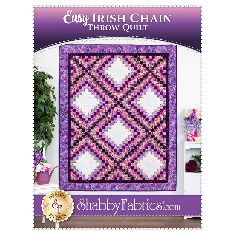 Front cover of the pattern showing the completed Easy Irish Chain Throw Quilt in vibrant shades of purple, magenta, and white, hung on a white paneled wall and staged with coordinating furniture and decor.