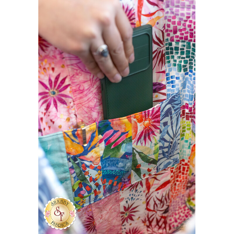 A model puts away a phone into the completed Coming Up Roses Jelly Roll Tote, demonstrating the patchwork of the project as well as the roominess of the project.