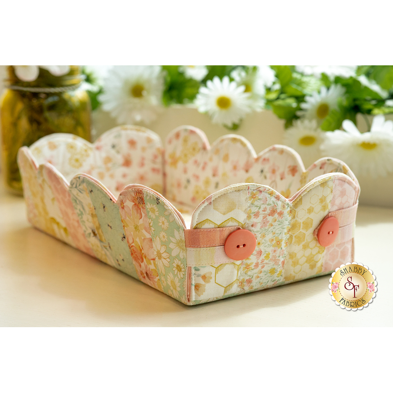 The completed scalloped basket in pastel yellow, pink, green, and soft white fabrics, staged on a countertop with coordinating flowers and decor.