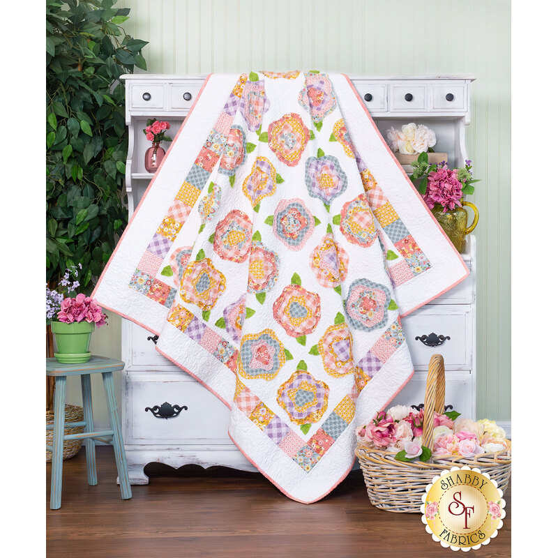 The completed French Roses quilt in the Nature Sings collection from Poppie Cotton, artfully draped over a rustic white armoire staged with coordinating flowers and decor.