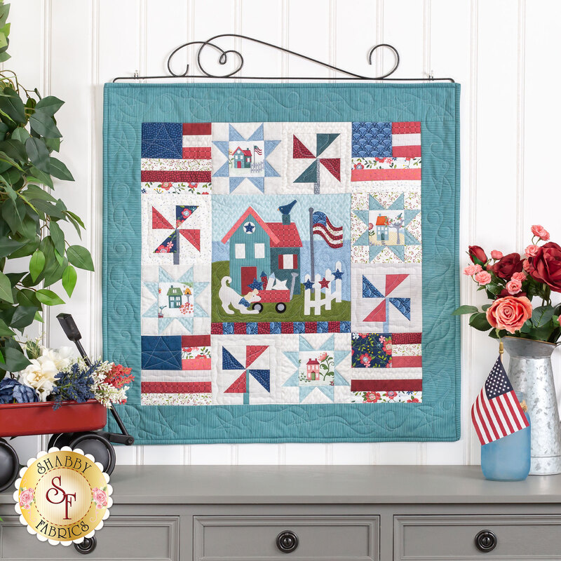 The completed Liberty Heights wall hanging, hung on a white paneled wall and staged with coordinating flowers and an American flag.