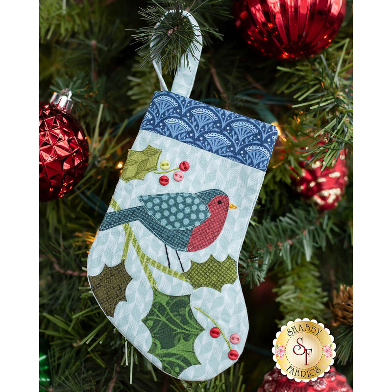 The completed Holly Bird stocking, hung on a green Christmas tree decorated with red bulbs.