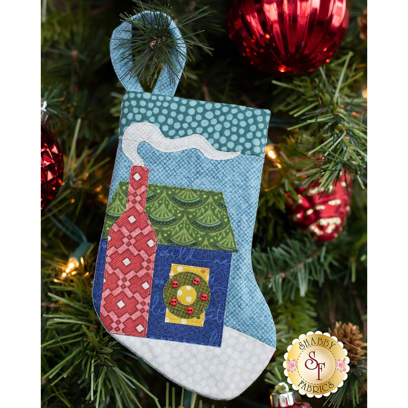 The completed Home stocking, hung on a green Christmas tree decorated with red bulbs.