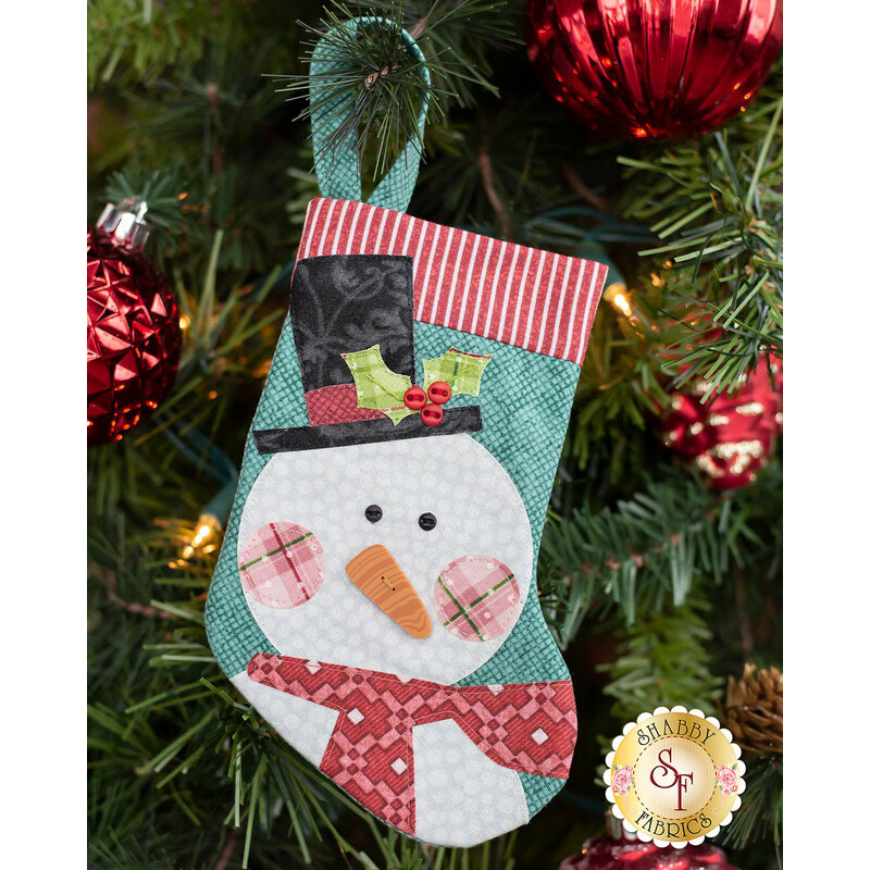 The completed snowman stocking, hung on a green Christmas tree decorated with red bulbs.