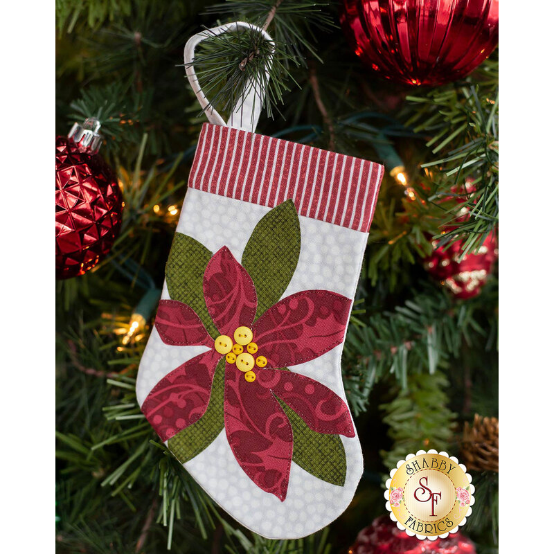 The completed poinsettia stocking, hung on a green Christmas tree decorated with red bulbs.