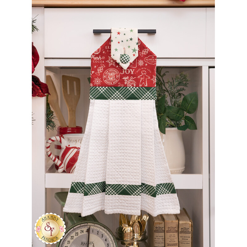 The completed hanging towel in red, hung from a kitchen drawer and staged with coordinating decor and greenery.