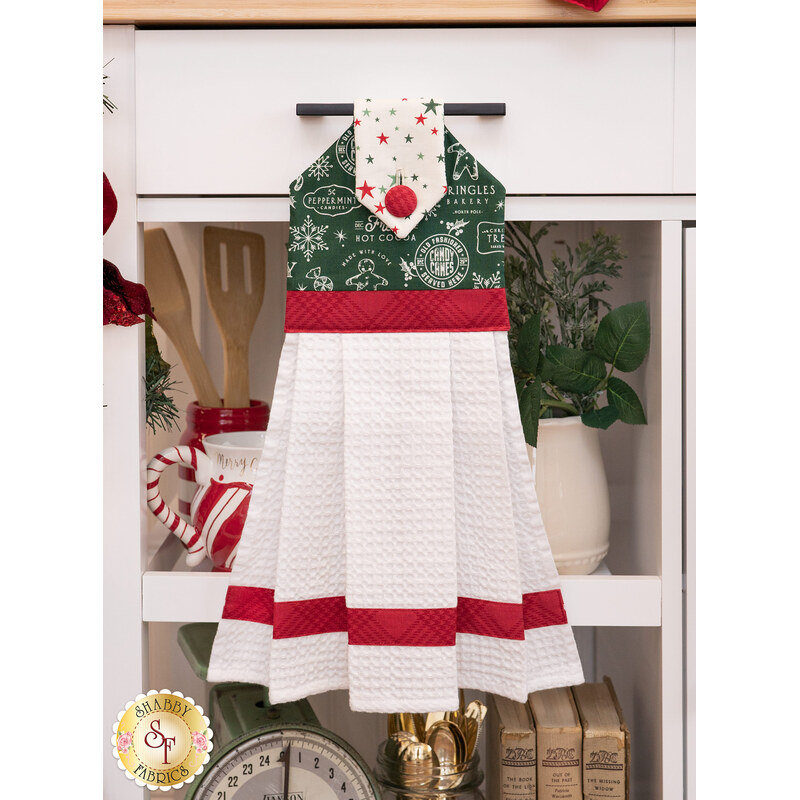 The completed hanging towel in green, hung from a kitchen drawer and staged with coordinating decor and greenery.