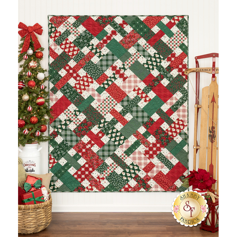 The completed Picnic quilt in green, red, and cream, hung on a white paneled wall and staged with coordinating furniture and decor.