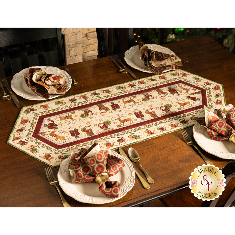 The completed table runner staged on a brown table with four plates set with silverware and coordinating Up On the Housetop napkins.