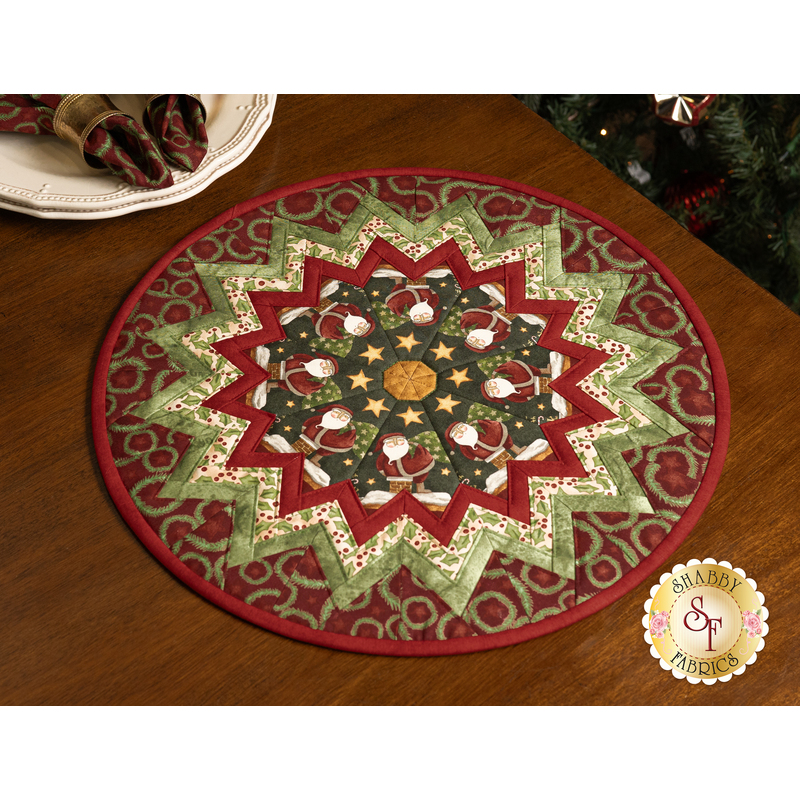 The completed Up On The Housetop Table Topper, colored in red, green, and cream, with coordinating napkins on a plate in the top left corner, staged on a brown table.