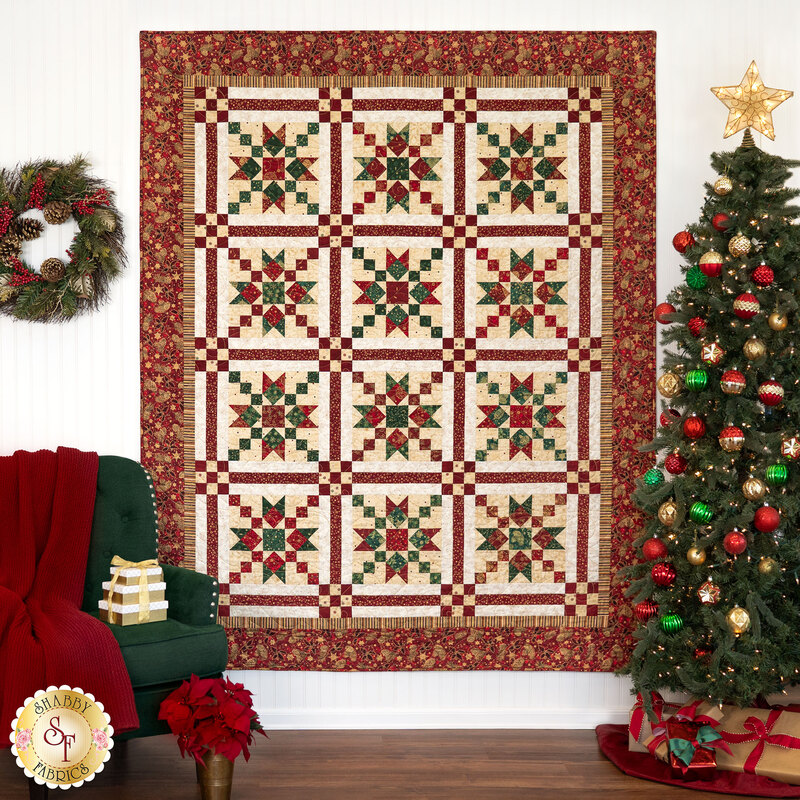 The completed Christmas in Coeur d'Alene quilt, colored in Christmas red and green with cream and gold accents, hung on a white paneled wall and staged with coordinated decor.