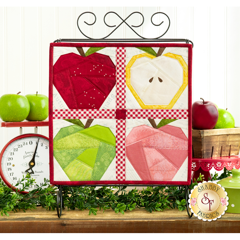 The completed Foundation Paper Piecing September project, colored in a bright palette, staged on a rustic wood set of drawers with coordinating apples and decor.