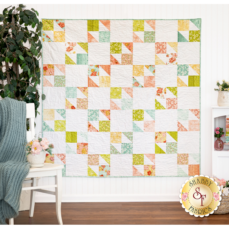 The completed Butterfly Patch quilt, colored in the Kindred collection from Moda Fabrics, hung on a white paneled wall and staged with coordinating decor.