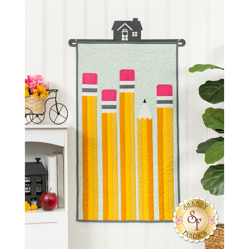 The completed September door banner project, five bright yellow number two pencils with pink erasers. The door banner is hung on a white paneled wall and staged with coordinating school themed decor. A leafy houseplant peeks into frame from the right side.