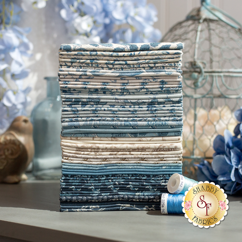 A stack of folded blue and cream patterned fabrics beside a spool of blue thread and flowers.