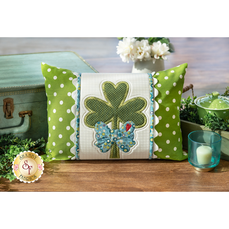 The finished March Pillow Wrap & cover, staged on a rustic wood floor beside a vintage suitcase and coordinating green decor.