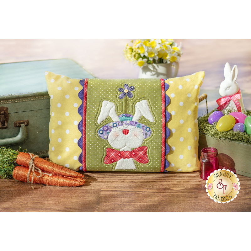 The finished April Pillow Wrap & cover, staged on a rustic wood floor beside a vintage suitcase and coordinating Easter decor.