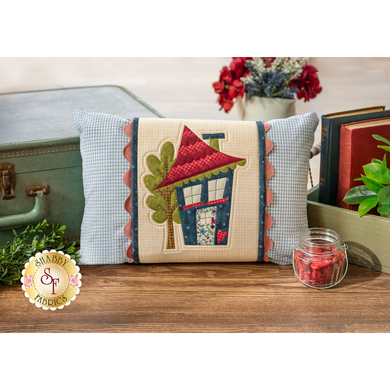 The finished June Pillow Wrap & cover, staged on a rustic wood floor beside a vintage suitcase and coordinating decor.