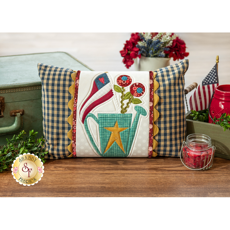 The finished July Pillow Wrap & cover, staged on a rustic wood floor beside a vintage suitcase and coordinating decor.