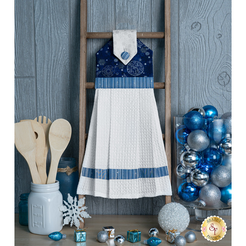 The completed hanging towel in dark blue, hung from a towel ladder rack on a kitchen counter and staged with coordinating decor.