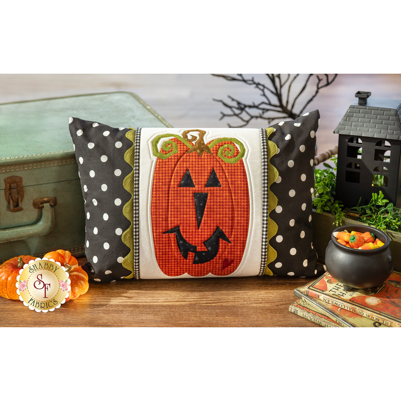 The finished October Pillow Wrap & cover, staged on a rustic wood floor beside a vintage suitcase, and coordinating Halloween decor.